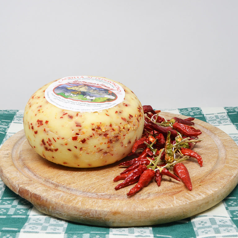 foto di un tagliere con una forma di caciotta al peperoncino di fianco ad un mazzo di peperoncini rossi secchi